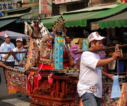 KAOHSIUNG, TAIWAN -- MARCH 16, 2014: Young men carry a sedan chair in which is seated the figure of a local deity at a  temple ceremony.