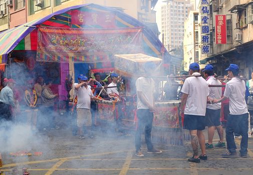 KAOHSIUNG, TAIWAN -- MARCH 16, 2014: Young men carry a sedan chair in which is seated the figure of a local deity at a  temple ceremony. The smoke is from firecrackers.