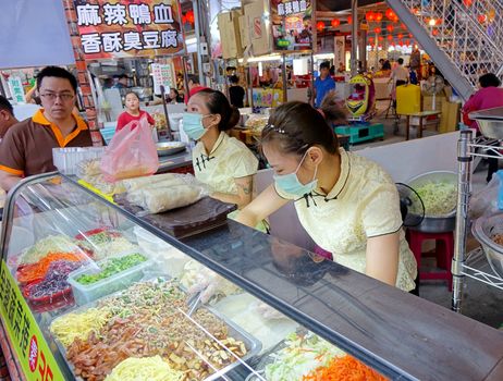 KAOHSIUNG, TAIWAN -- NOVEMBER 20, 2015: Two female shop assistents prepare spring rolls  filled with tofu and vegetables at the Jiangguo Outdoor Market.