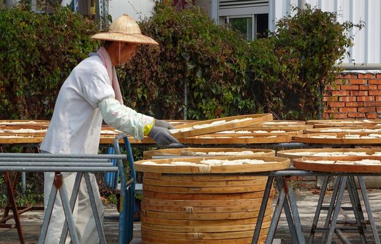 TAINAN, TAIWAN -- MARCH 4, 2014: An unidentified worker checks on noodles that are dried in the sun before packaging, a local specialty in southwest Taiwan.