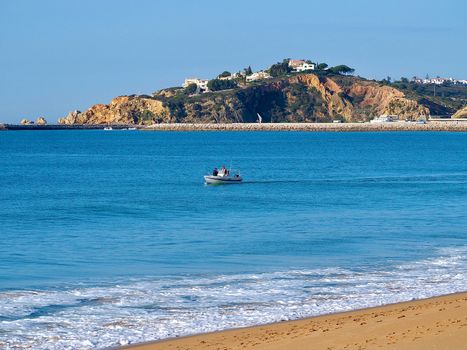 Coast of Albufeira with a fisher boat on blue sea