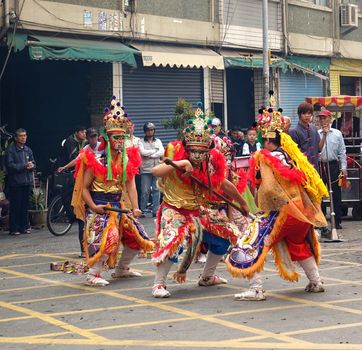 KAOHSIUNG, TAIWAN -- MARCH 16, 2014: Three young men with painted facial masks and dressed up as ancient warriors dance at a local temple ceremony.