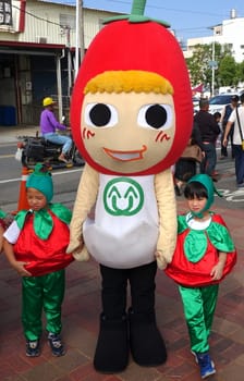 LUJHU, TAIWAN -- DECEMBER 12, 2015: A mascot dressed up as a cherry tomato poses with two children at the Lujhu Tomato Festival.

