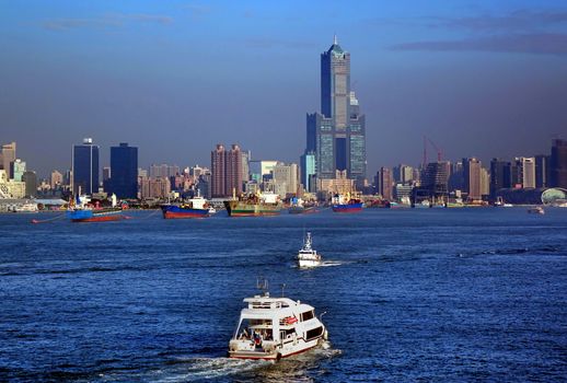 KAOHSIUNG, TAIWAN -- DECEMBER 22, 2018: Tourist boats take visitors on a cruise across Kaohsiung Port. In the back is the skyline of the city.
