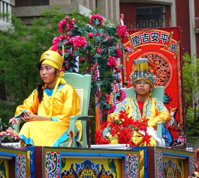 KAOHSIUNG, TAIWAN -- JULY 9, 2016: Young people in traditional Chinese costumes are seated on elevated chairs during religious Taoist procession.