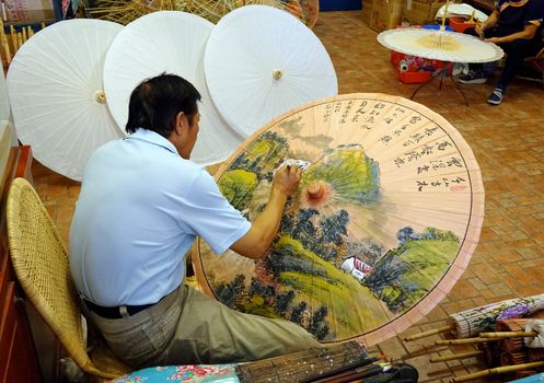 KAOHSIUNG, TAIWAN -- JULY 24, 2016: A male artist paints oil-paper umbrellas, which is a traditional art and craft product by the Chinese Hakka people.