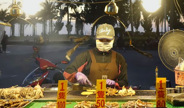 KAOHSIUNG, TAIWAN -- DECEMBER 22, 2018: A street vendor cooks grilled squid near the beach on Cijin Island.
