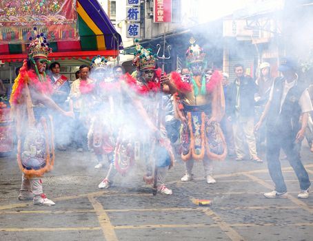 KAOHSIUNG, TAIWAN -- MARCH 16, 2014: Three young men with painted facial masks and dressed up as ancient warriors pose at a local temple ceremony amidst smoke from fireworks.