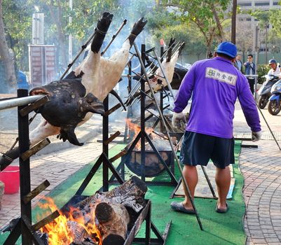 KAOHSIUNG, TAIWAN -- FEBRUARY 9, 2019: A member of Taiwan's indigenous people roasts whole pigs on the banks of the Love River during the Lantern Festival.
