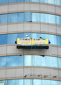 KAOHSIUNG, TAIWAN -- JUNE 27, 2014: Two unidentified workers perform the dangerous task of washing the windows of an office tower