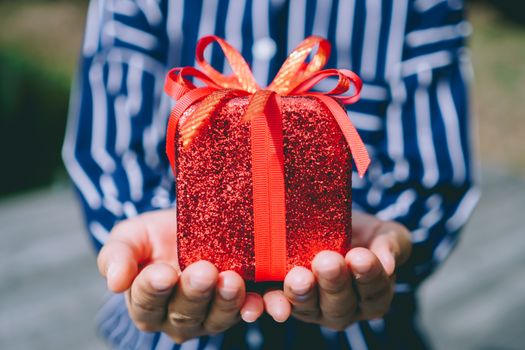 Hand hold gift box to someone on green bokeh nature. Celebration holiday concept.