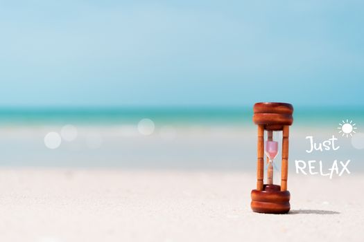 Just relax qoute with hourglass on sand and summer beach blue sky background. Time to travel tourism season concept background.