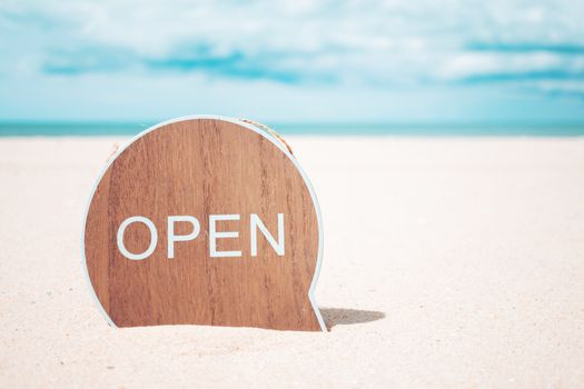 Now open sign board stand on sand summer beach background metaphor to time to travel relax tourism season with copyspace background.