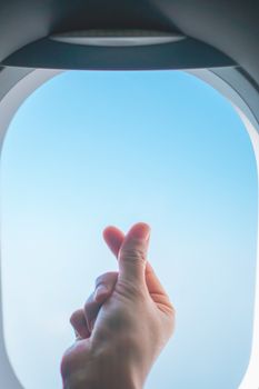 Love symbol of korean with your fingers cross. A female hand depicts a heart in front of window of airplane.  Freedom travel concept.