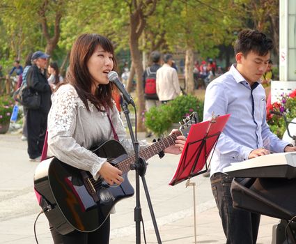 KAOHSIUNG, TAIWAN -- MARCH 23, 2014: Two young unidentfied musicians busk outdoors in the Central Park of Kaohsiung