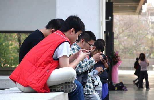 KAOHSIUNG, TAIWAN -- FEBRUARY 19, 2015: Young people are deeply absorbed with their mobile devices, seemingly oblivious to their surroundings. 
