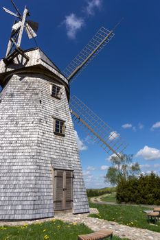 Old windmill in a country landscape with woodland trees under a cloudy blue sky in a scenic landscape