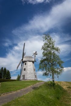 Picturesque empty country road leading to an old tower mill in rural area. Countryside landscape shot from low angle against blue sky