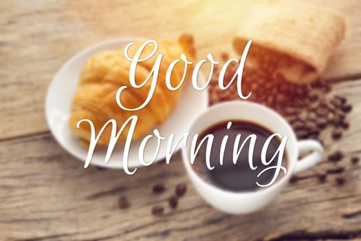 text good morning with blurry of continental breakfast with fresh croissant and hot coffee on wooden table, decoration with coffee bean as background