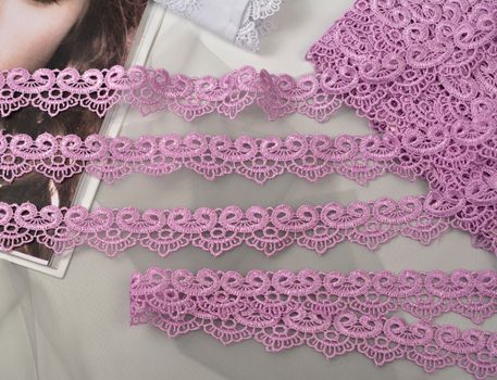 Tapes of pink gentle guipure, beauty lace fabric on light background. Elastic material. Using for Atelier and needlework store.