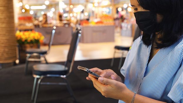 Asian woman using smartphone and sitting separated chair in shopping mall for social distancing to protect covid-19 and coronavirus outbreak, a new normal lifestyle concept