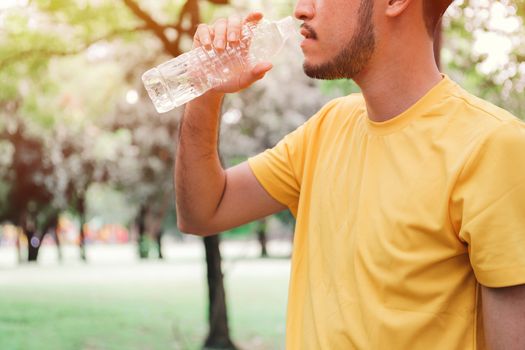 Young asian man jogger drinking water from the bottle after hard exercise in the garden, healthy concept