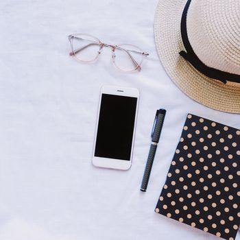 Top view of accessories, hat, eyeglasses, notebook and smartphone on white background, lifestyle concept