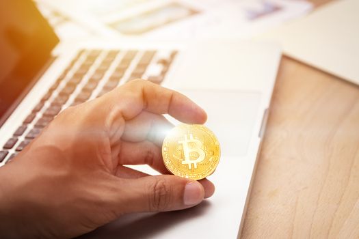 businessman holding cryptocurrency golden bitcoin coin in hand with computer laptop at background. crypto currency, electronic virtual money for web banking and international network payment