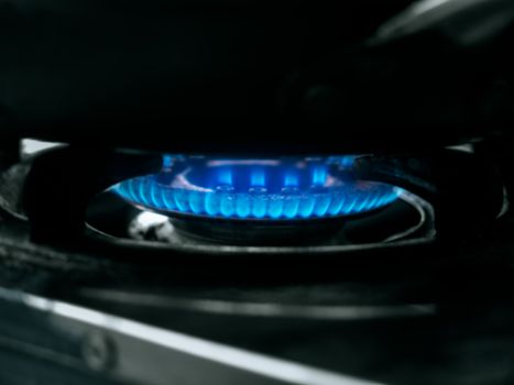 Blurred background of blue flame burning by kitchen gas cooker. Close-up blurry gas burner with blue fire.