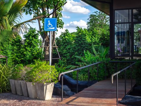 Disabled way sign in front of cafe on green nature landscape background. Wheelchair ramp way with disabled sign for support wheelchair disabled people.