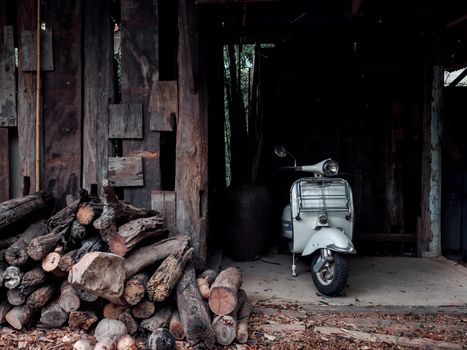 KHON KAEN, THAILAND - June 1, 2020: White vintage Vespa motor scooter parking in wood cabin near the piles of firewood in countryside in Thailand.