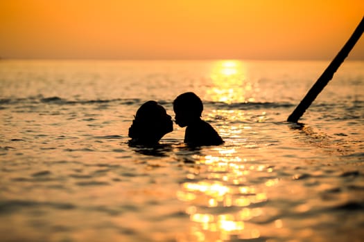 Silhouette mother and child are kissing in the sea while the sunset.