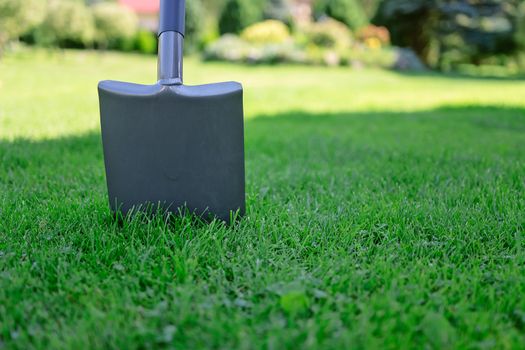 Garden shovel stuck in green grass in close-up (copy space)