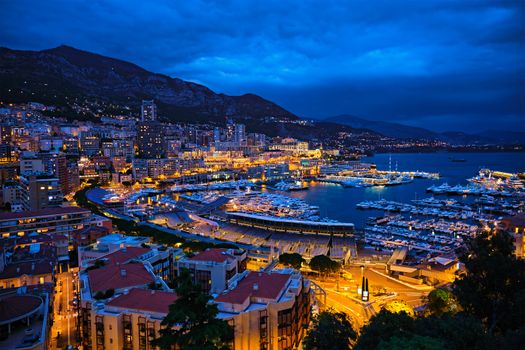 Aerial view of Monaco Monte Carlo harbour and illuminated city skyline in the evening blue hour twilight. Monaco Port night view with luxurious yachts