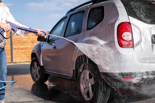 The woman is holding a lance in her hand and washes her car under high pressure with water and shampoo