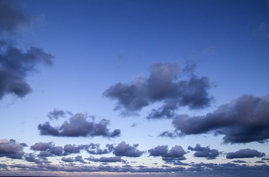 Impressive sky at sunset with layers of clouds tinged with pink that slope down towards the horizon