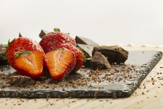 Neatly placed strawberries on a slate plate with chopped chocolate and grated around on a light wooden background and selective focus