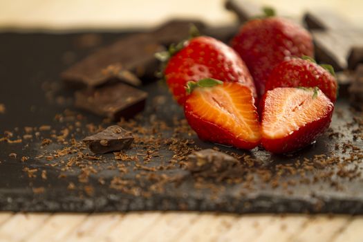 Neatly placed strawberries on a slate plate with chopped chocolate and grated around on a light wooden background and selective focus
