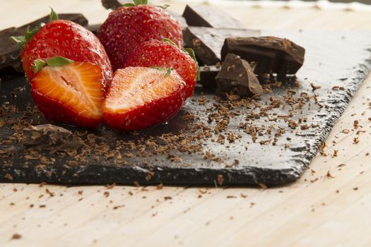 Neatly placed strawberries on a slate plate with chopped chocolate and grated around on a light wooden background and selective focus