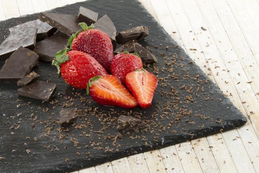 Neatly placed strawberries on a slate plate with chopped chocolate and grated around on a light wooden background and selective focus