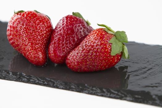 Close-up of three isolated strawberries on a rectangular strip of diagonally wet slate on a white background shot in high angle view 