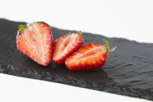 Close-up of three isolated strawberries on a rectangular strip of diagonally wet slate on a white background shot in high angle view with selective focus