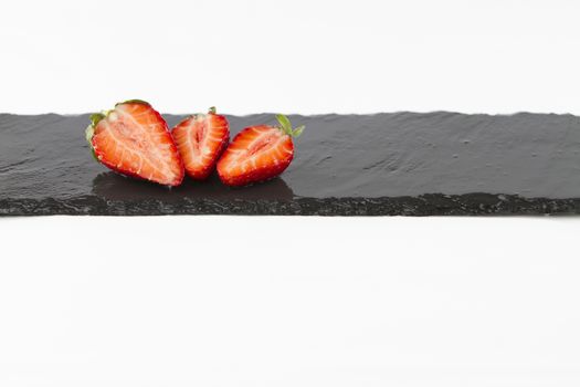 Close-up of three isolated strawberries on a rectangular strip of wet slate on a white background shot in high angle view with selective focus