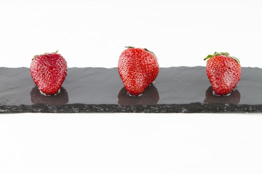 Close-up of three isolated strawberries on a rectangular strip of wet slate on a white background shot in high angle view with selective focus