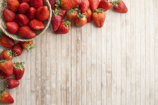 Strawberries copy space with a small basket of strawberries in the upper left corner surrounded by strawberries scattered on a wooden background taken from above