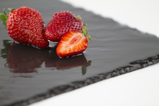 Close-up of three strawberries isolated on a wet square slate plate on a white background shot in high angle view with selective focus