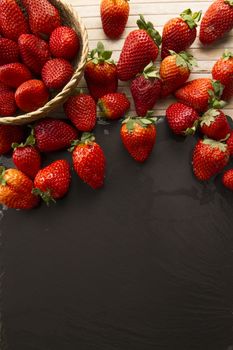 Strawberries copy space with a small basket of strawberries surrounded by strawberries scattered on a wooden bottom and a plate of slate taken from above