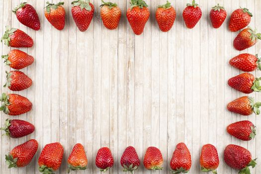 Strawberries copy space with strawberries all along the perimeter to form a rectangle on a background of light wood taken from above