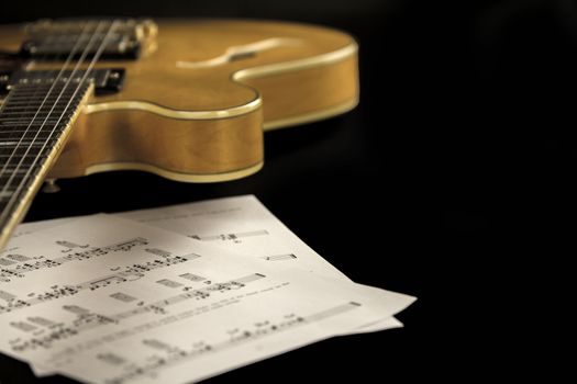 Vintage archtop guitar in natural maple close-up high angle view with music sheets on black background