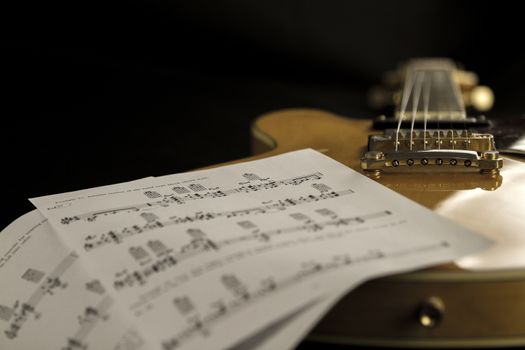 Vintage archtop guitar in natural maple close-up high angle view with music sheets on black background